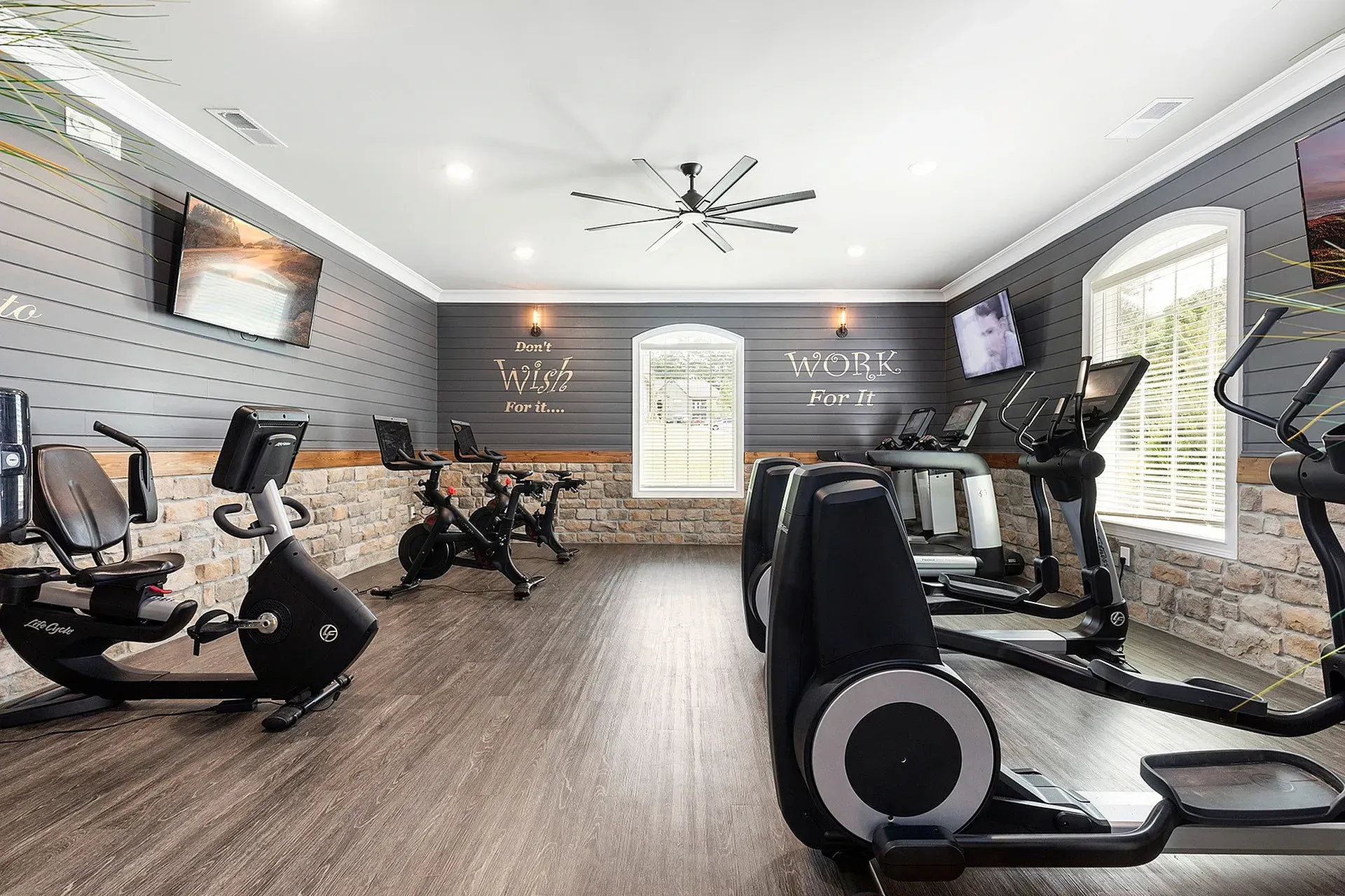 Indoor community gym featuring cardio machines (treadmills, bikes) and wall-mounted TVs.