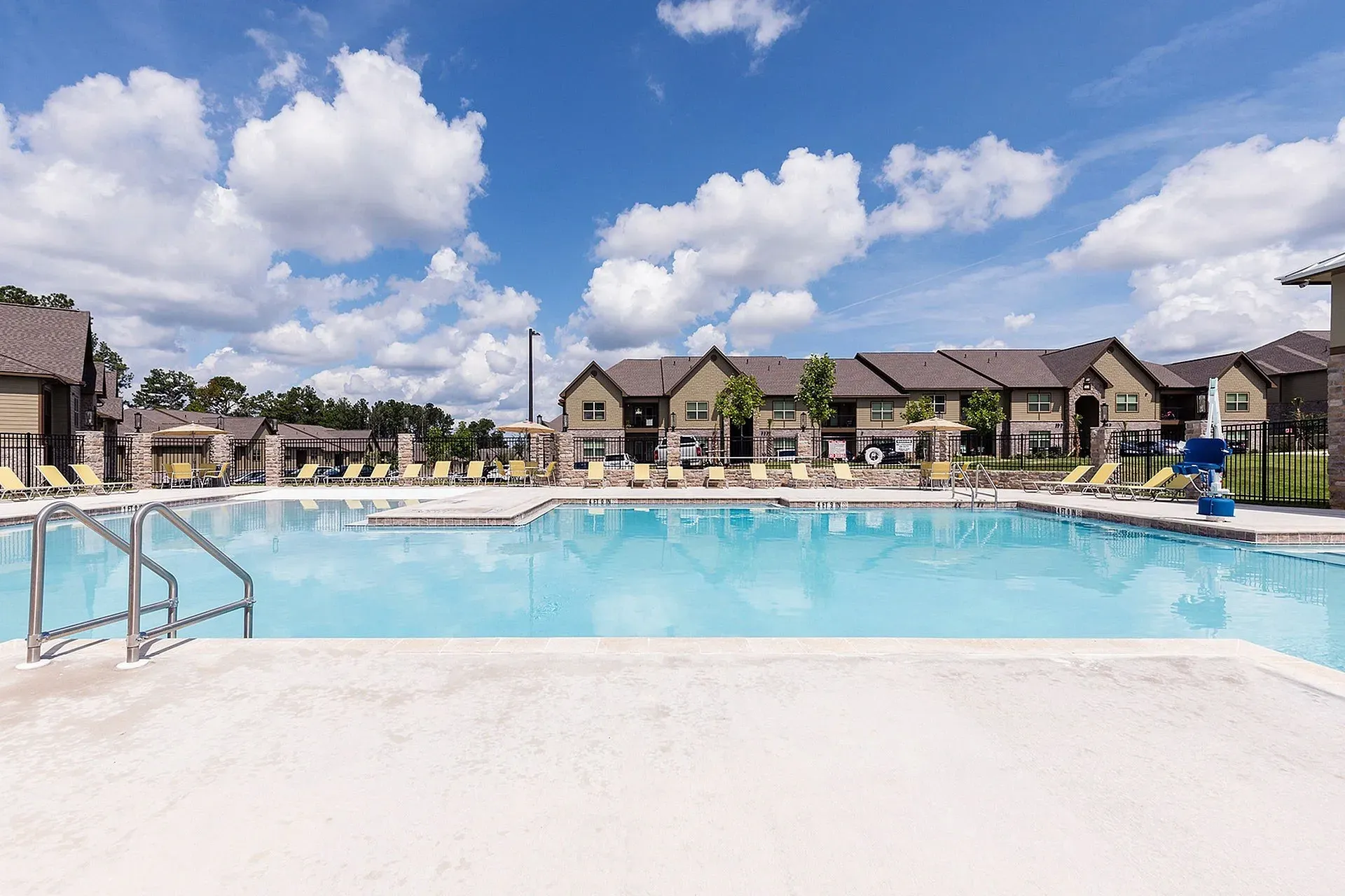 Outdoor apartment community pool with lounge chairs, surrounding buildings, and clear blue sky.