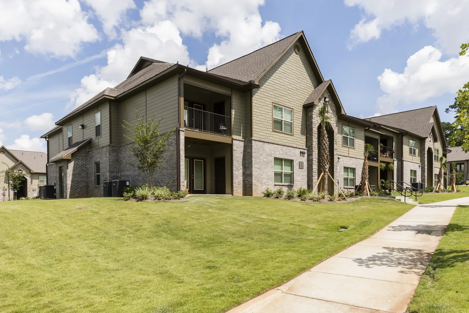 Exterior view of a modern apartment building with a green lawn and sidewalk.