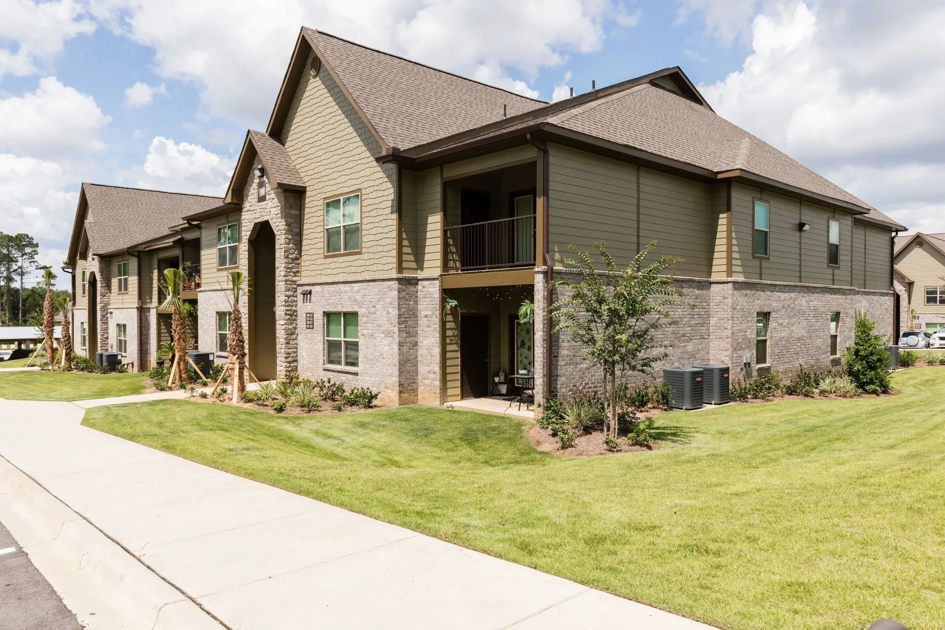 Exterior view of a modern apartment building with stone accents and a green lawn.
