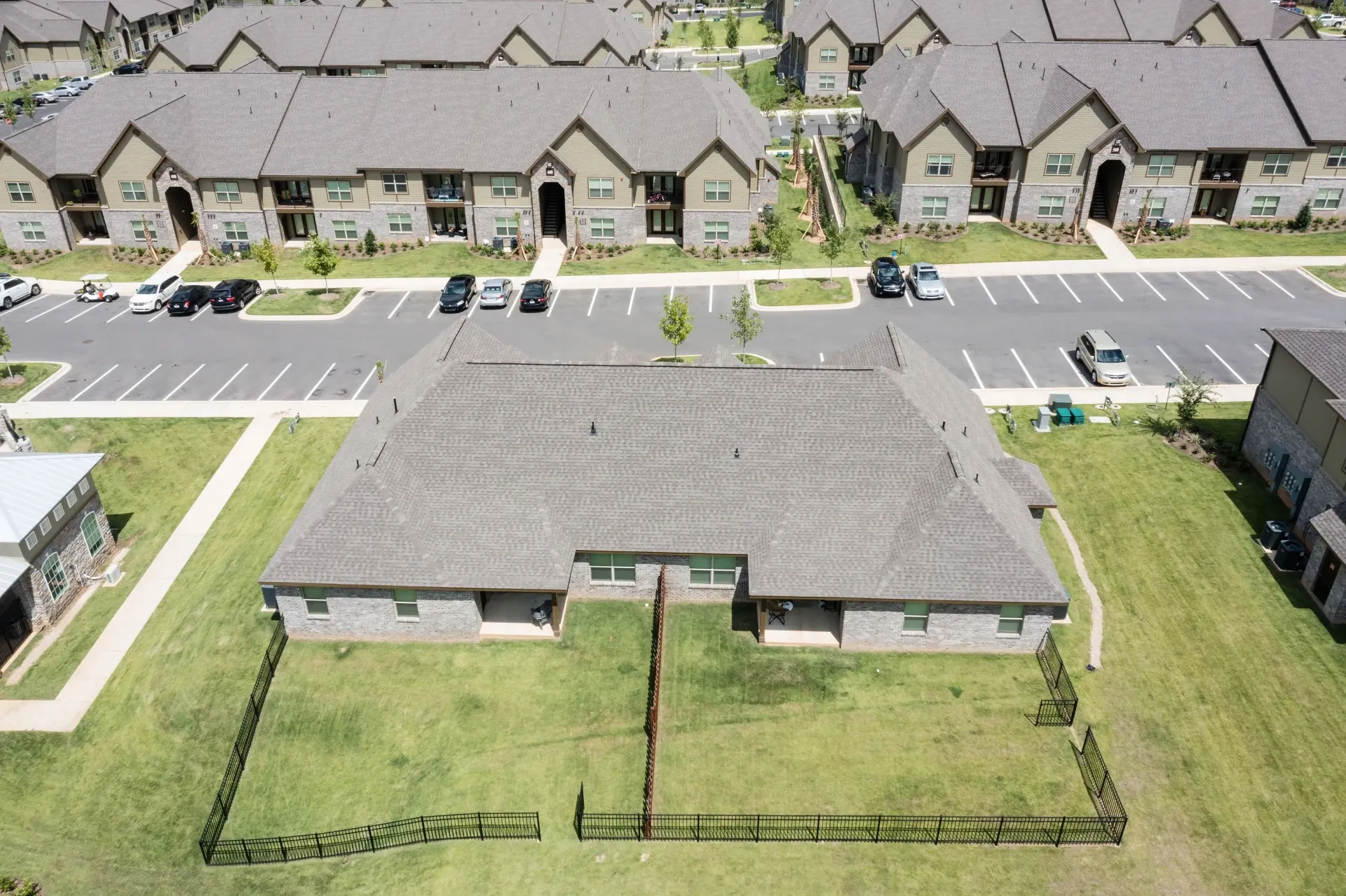Aerial view of a multi-building apartment community with parking lots, green lawns, and a central fenced yard.