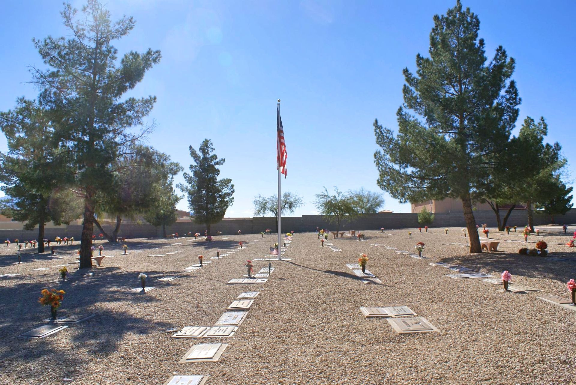 Cemetery with gravestones, trees, and an American flag on a sunny day.