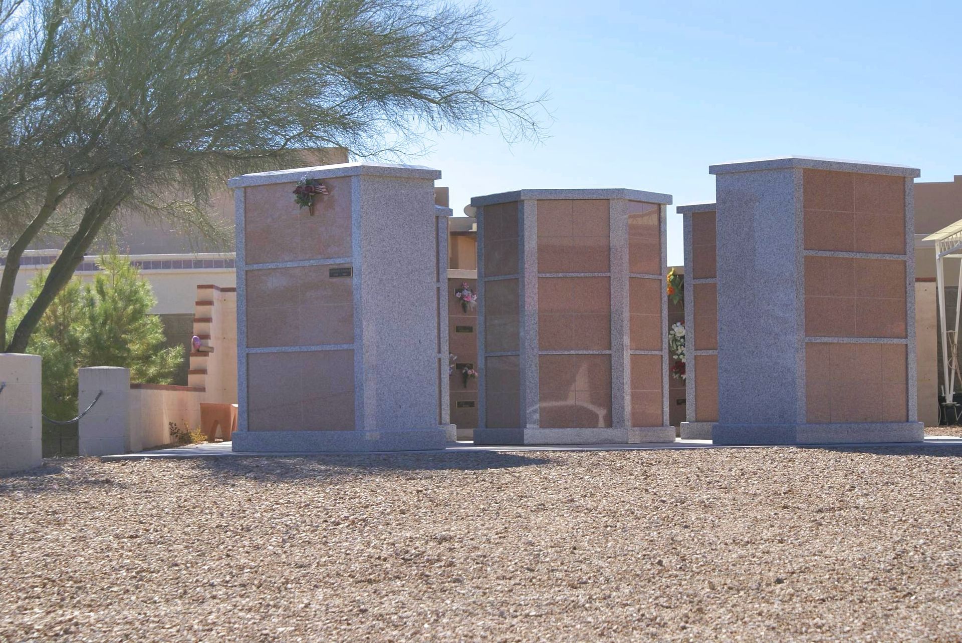 Row of columbarium niches in a sunny outdoor setting, made of granite and bronze.