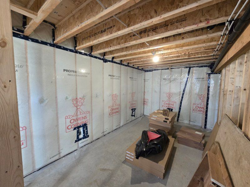 Unfinished basement with insulated walls, exposed ceiling joists, and construction materials on the floor