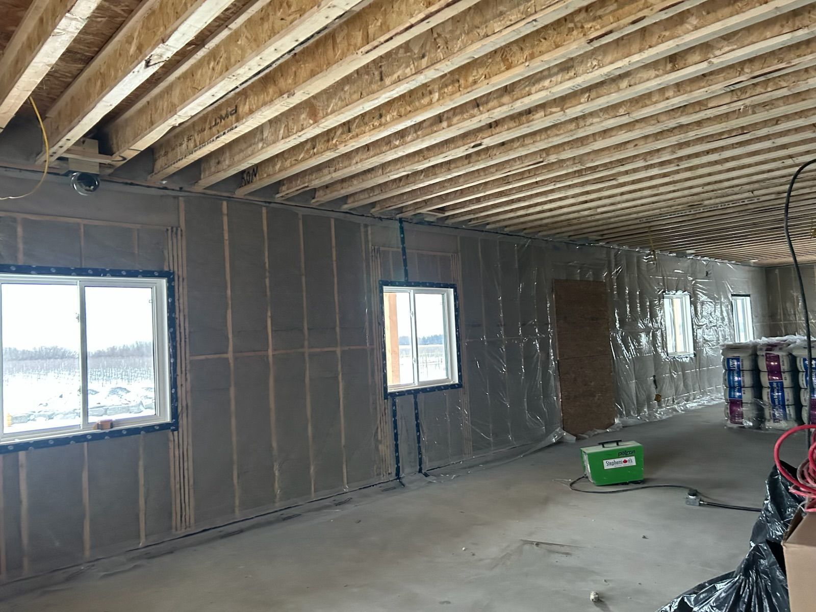 Unfinished basement with exposed ceiling joists, framed walls, two windows, and construction materials on the floor