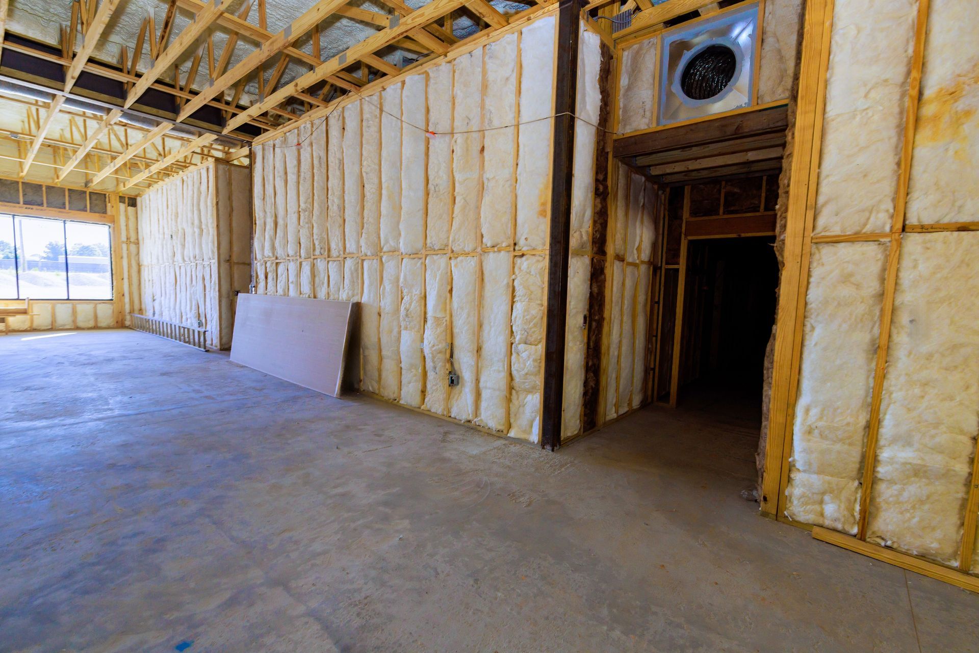 Unfinished room with spray foam insulation, exposed ceiling beams, concrete floor, and doorway to a dark hallway