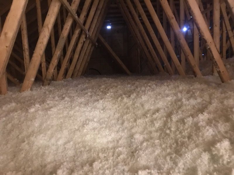 Attic with exposed wooden beams and a thick layer of white insulation on the floor