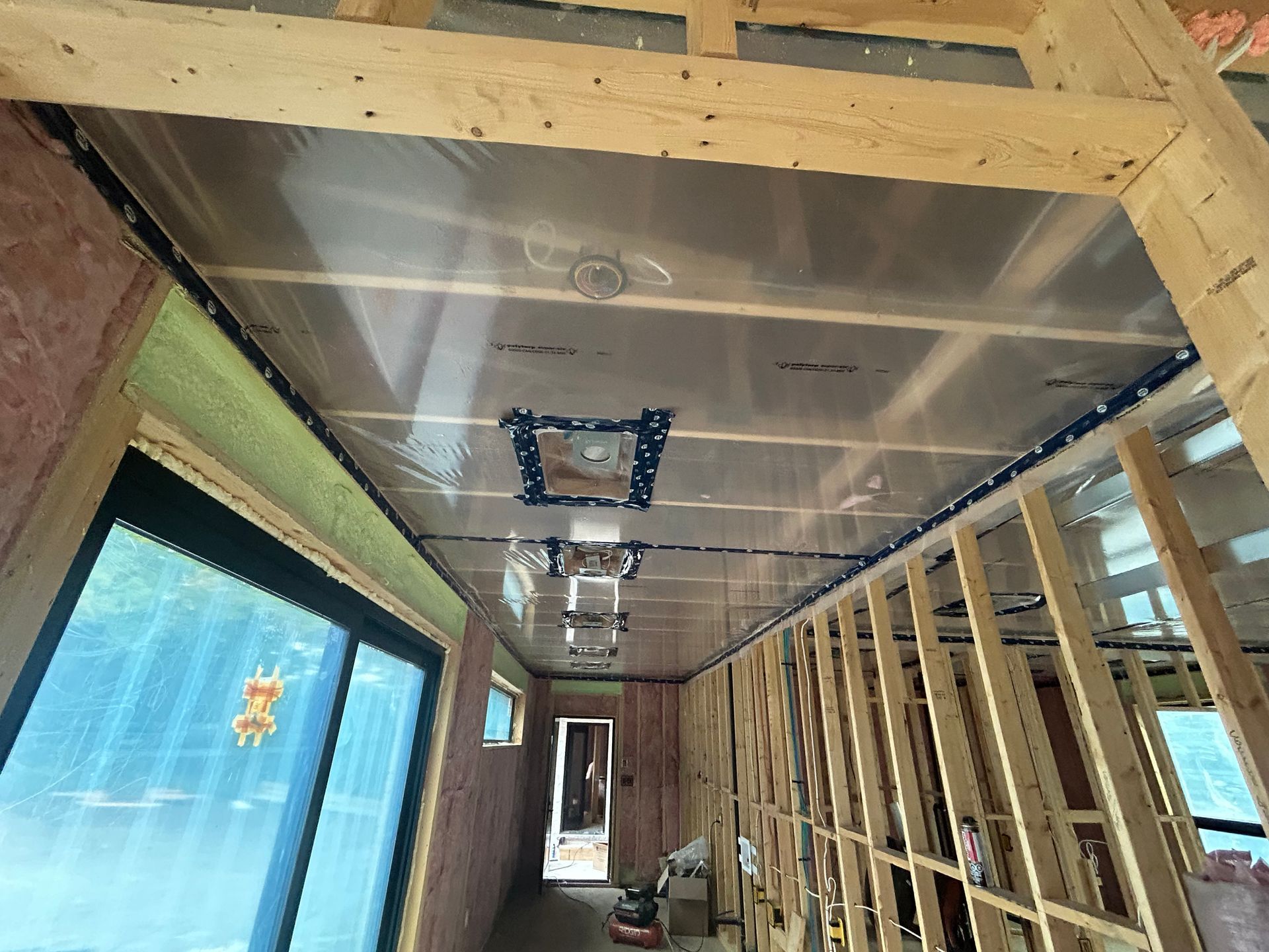 Unfinished hallway under construction with exposed framing, insulation, and ceiling panels along a narrow corridor.