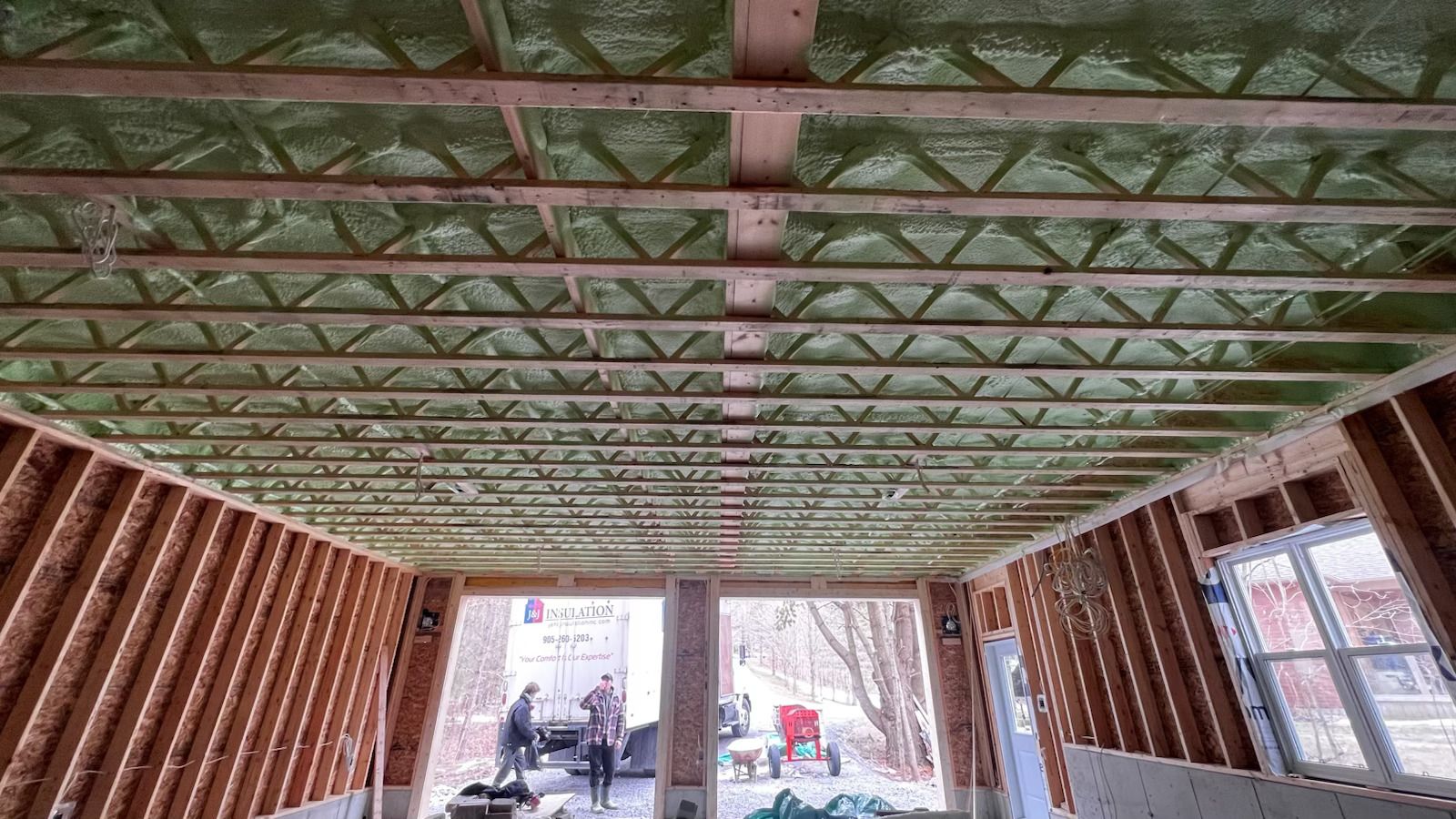 Interior of a partially built room with exposed wood framing and a green ceiling grid, seen from the center