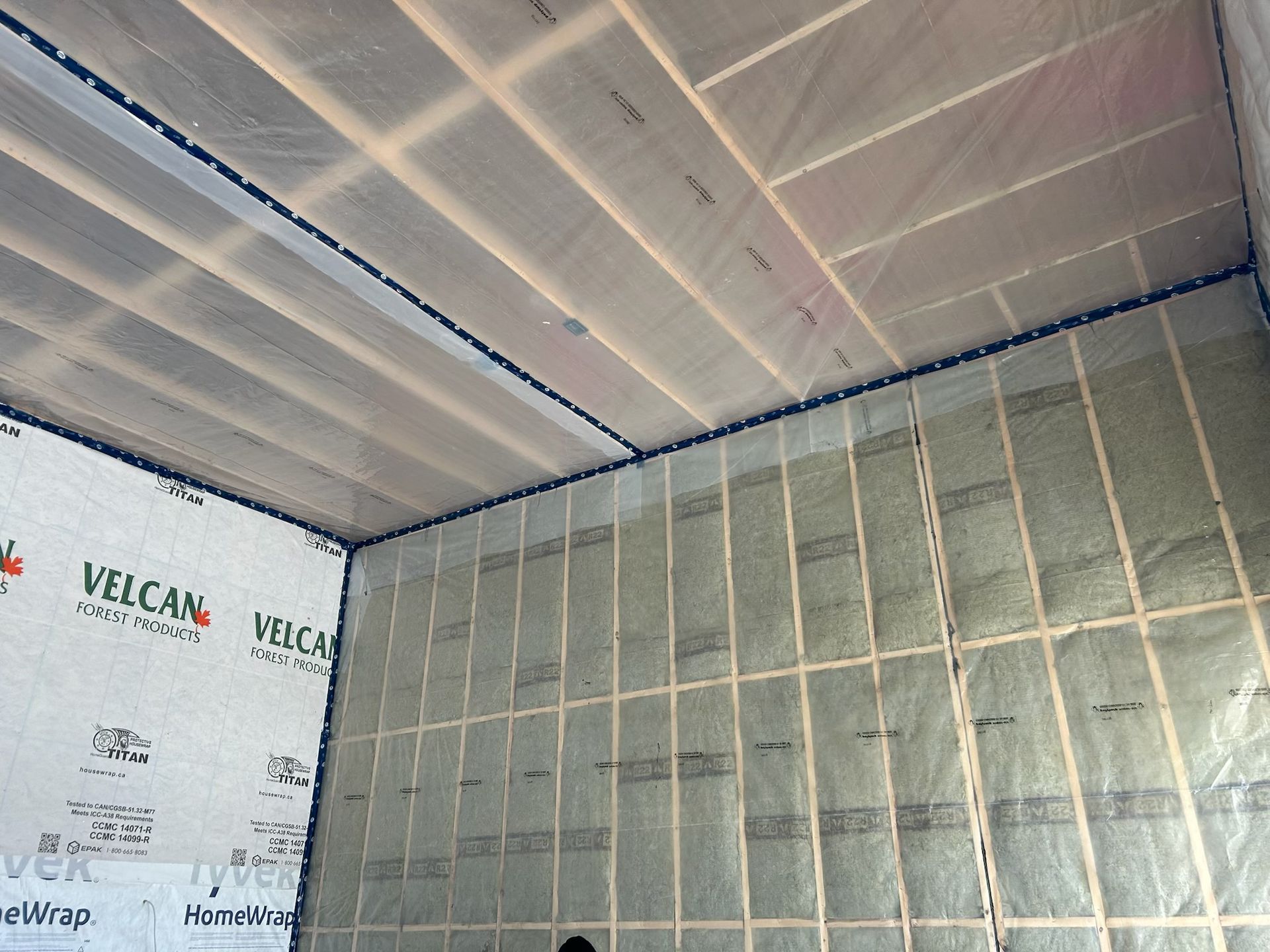 Interior wall and ceiling insulation installation with white plastic sheeting and exposed framing