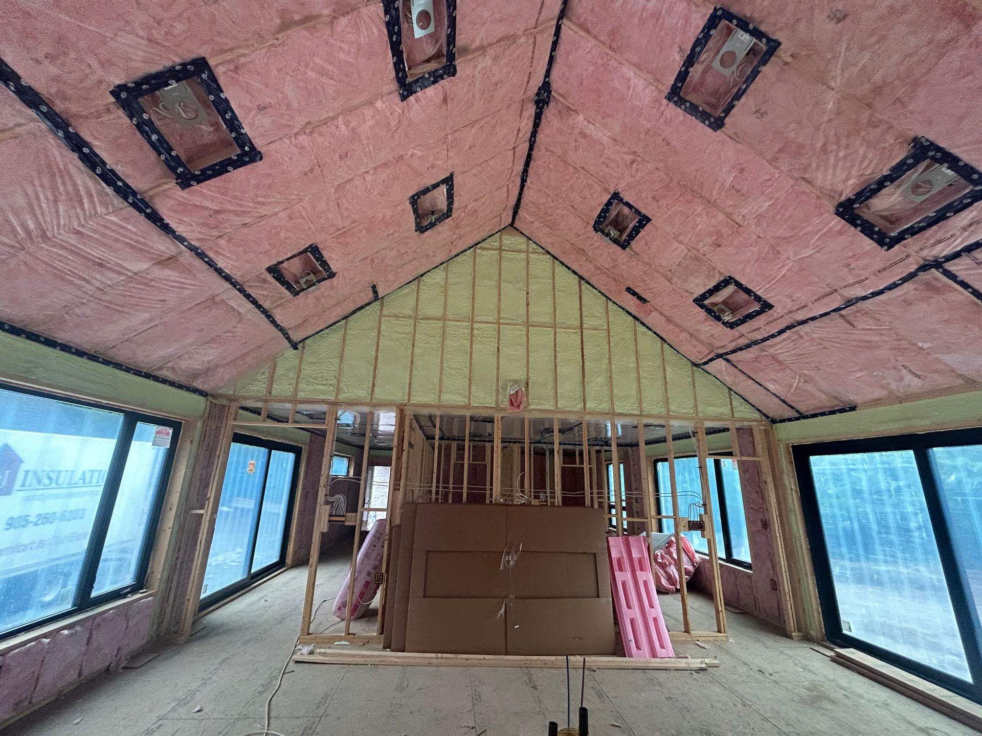 Unfinished attic room with pink insulation, exposed framing, and large windows on both sides.