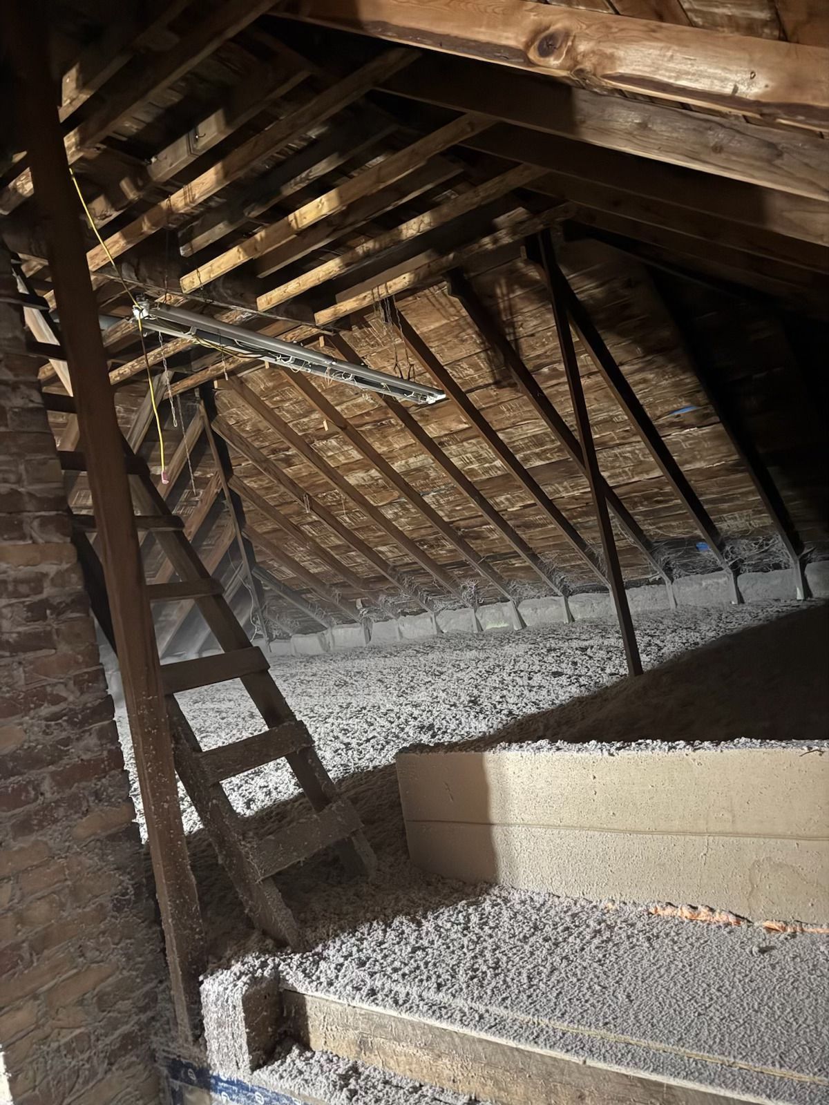 Attic with exposed wooden rafters, brick wall, and gravel-covered floor under a steep roof
