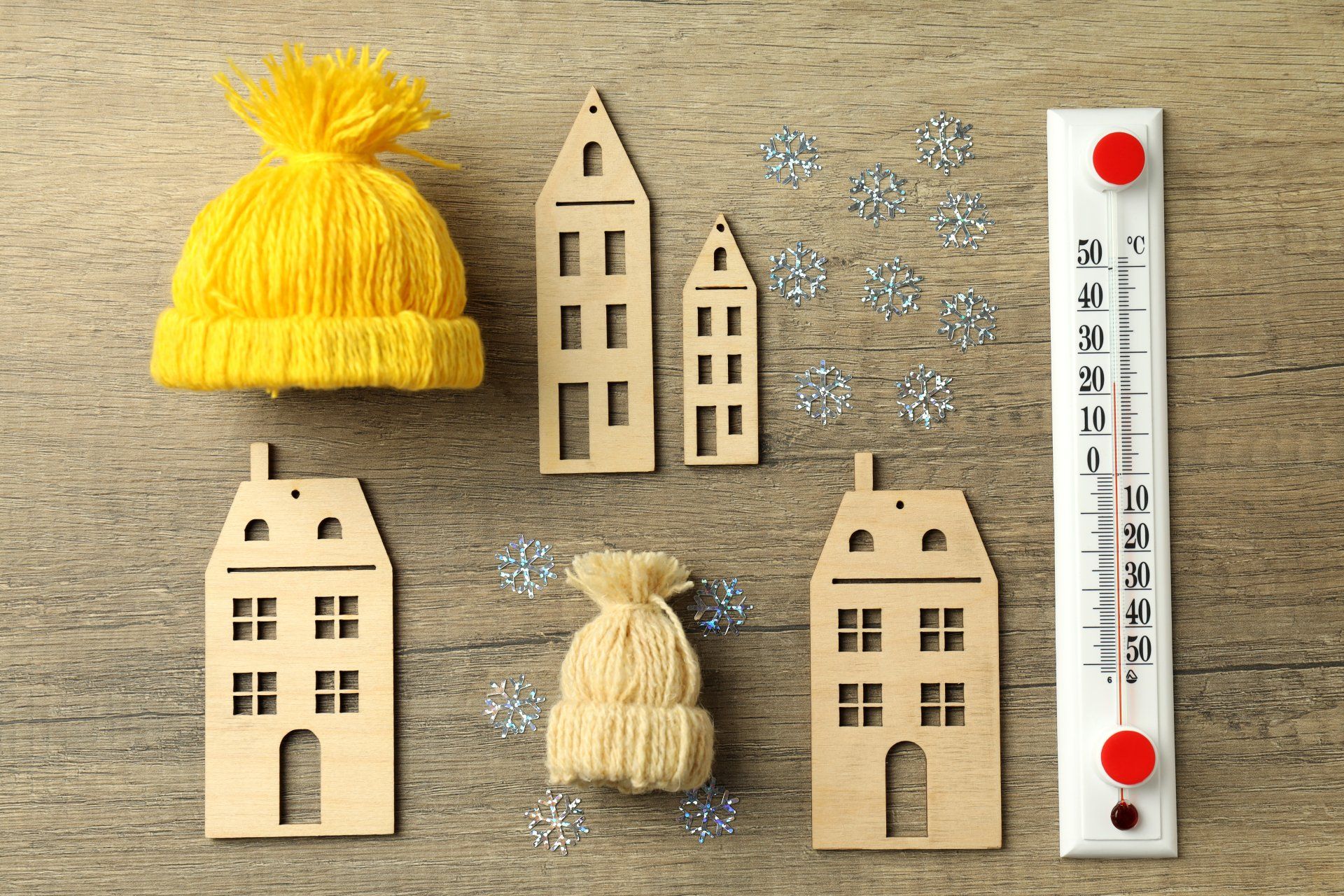 Knitted hats, wooden houses, snowflakes, and a thermometer on a beige background