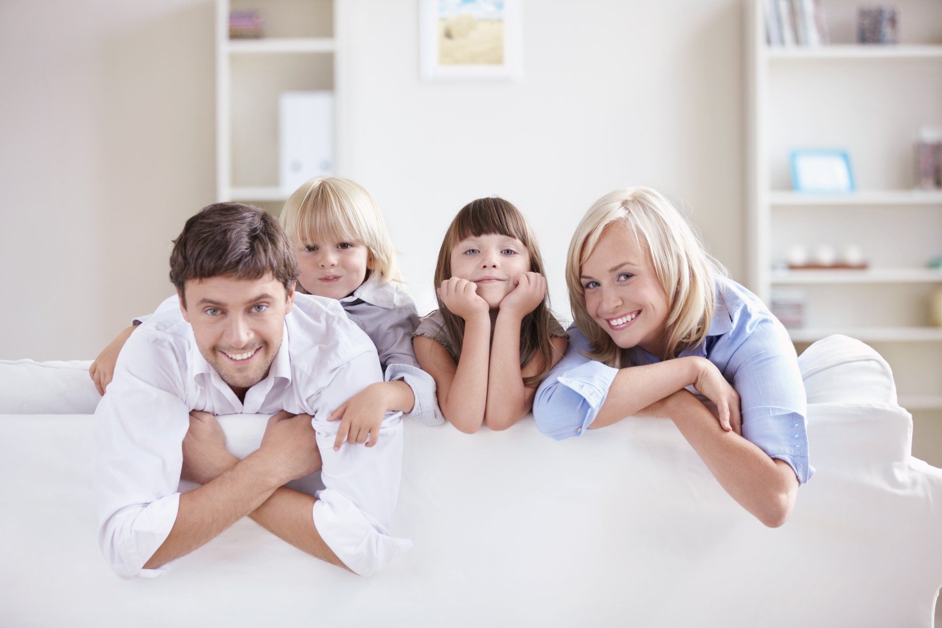 Family of four smiling on a white couch in a bright living room