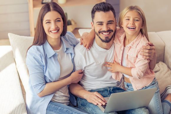 Smiling family sitting on a couch with a laptop in a bright living room