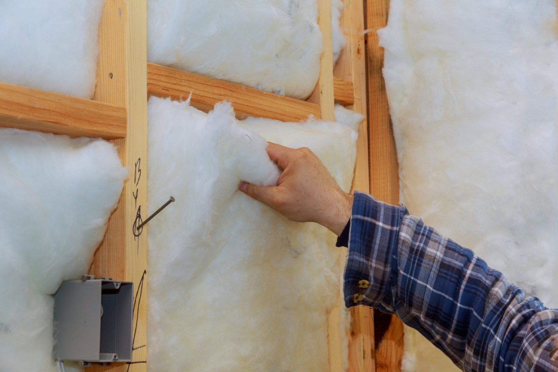 Hand placing white insulation batt into a wooden wall frame during construction