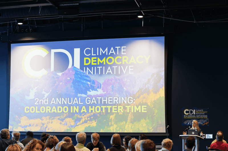 Climate Democracy Initiative event stage with large blue banner reading “2nd Annual Gathering: Colorado in a Hotter Time”
