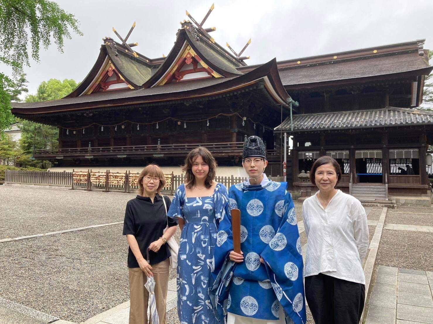 Four people posing in front of a traditional Japanese building, one in a blue kimono-style outfit.
