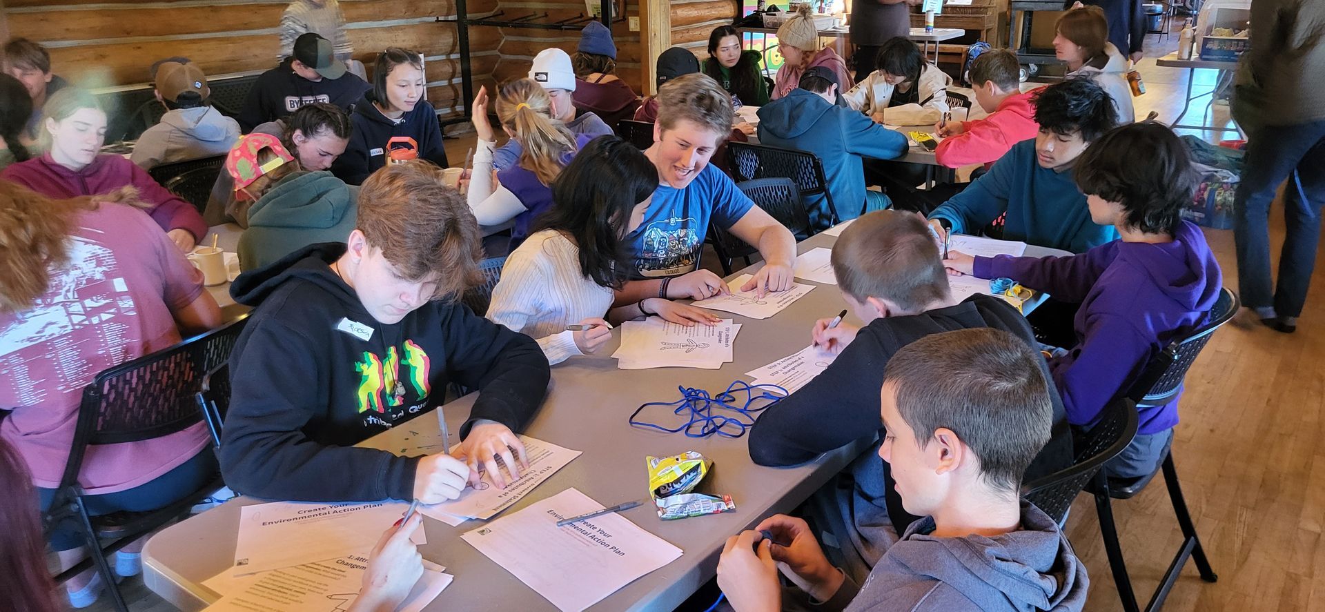 Students seated at tables, working on a hands-on classroom activity with papers and small materials