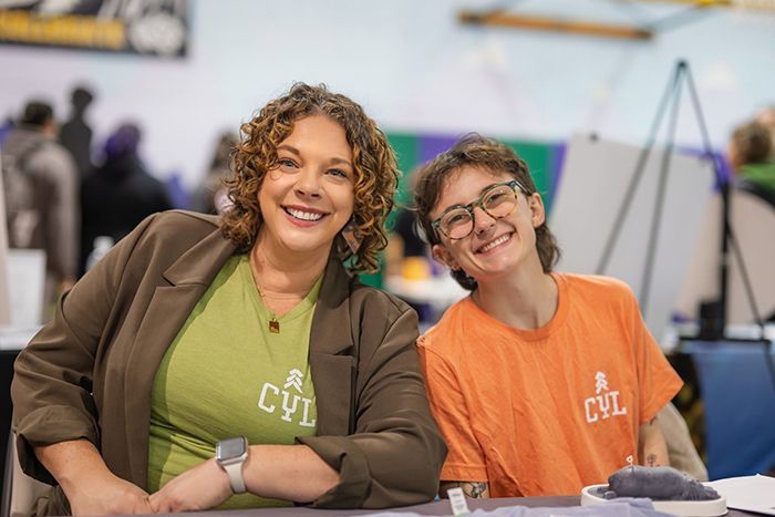 Two smiling volunteers in green and orange shirts sitting at a table indoors