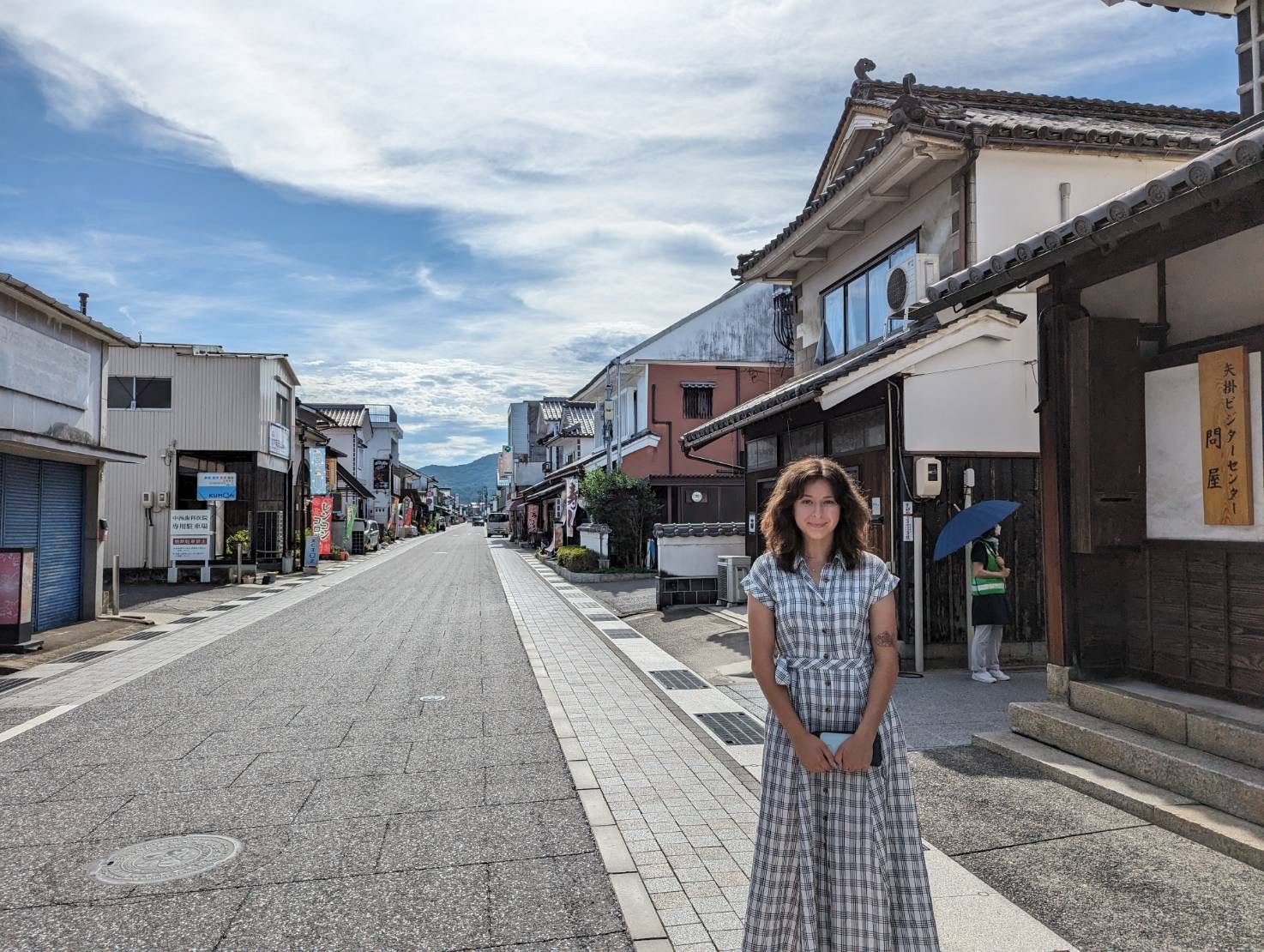 Woman standing on a quiet street lined with traditional buildings under a blue sky