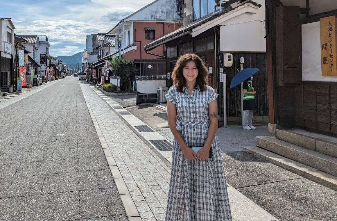 Woman standing on a cobblestone street in a small town, with shops and buildings lining both sides.