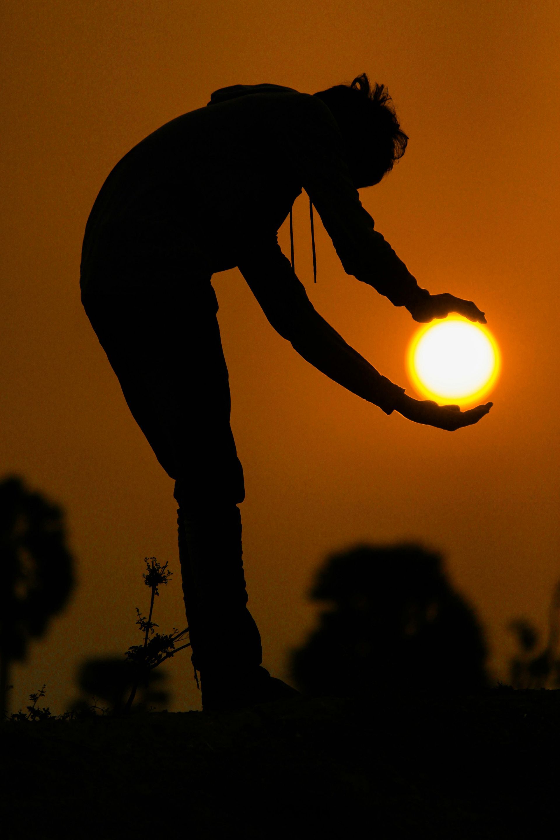 Silhouette of a person holding the sun at sunset against an orange sky