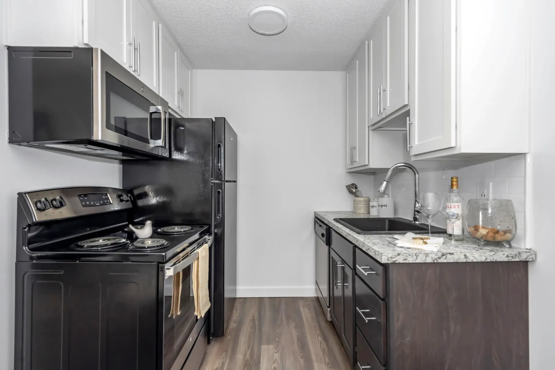 Compact modern kitchen with black appliances, white cabinets, and gray countertops
