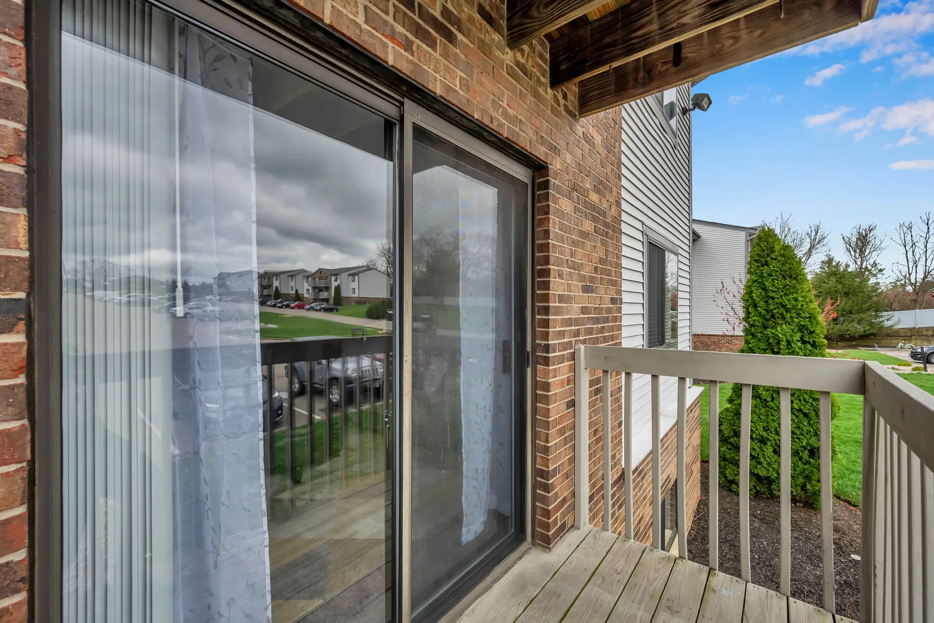 Balcony with sliding glass door, brick wall, and railing overlooking a grassy yard
