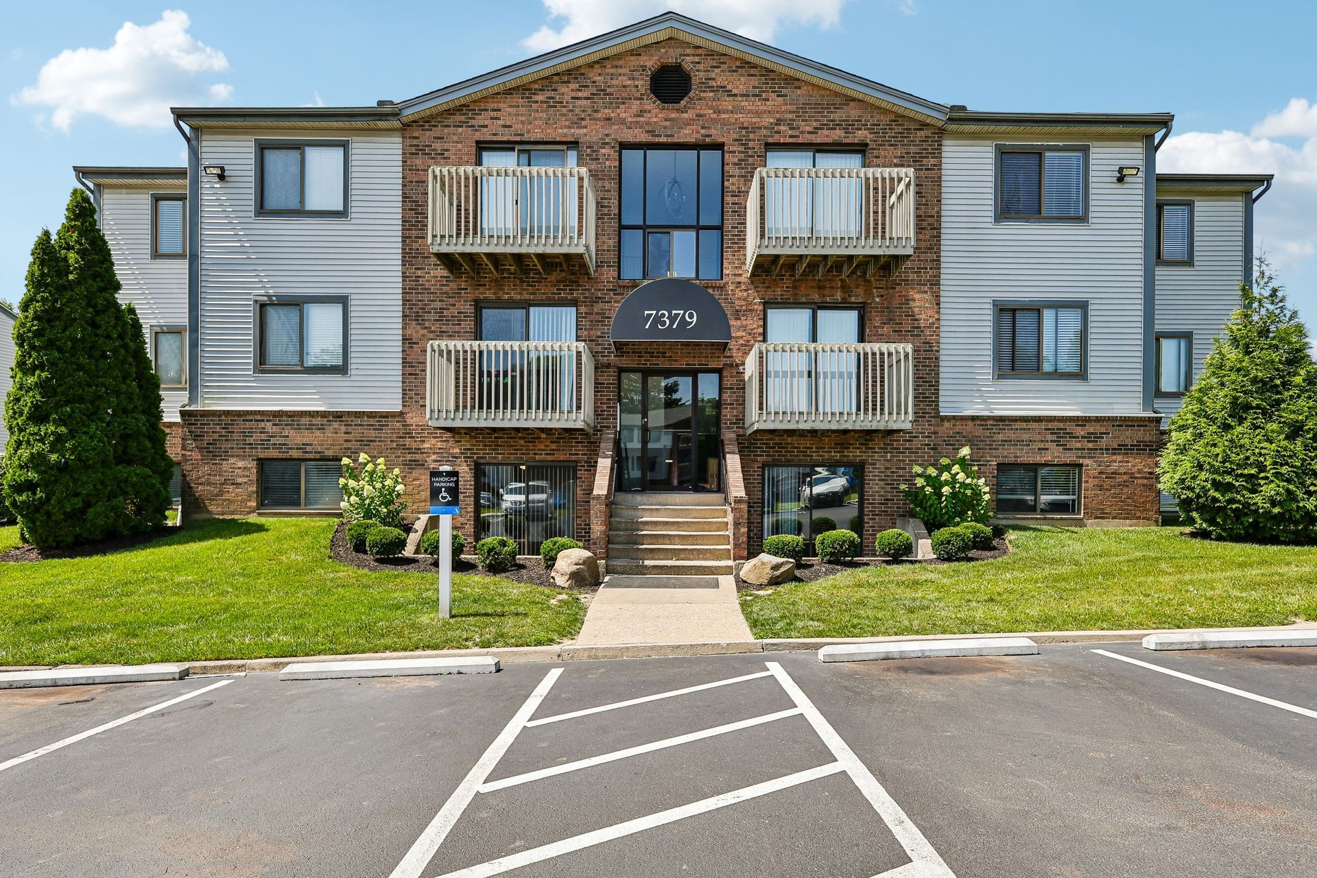 Tall Timber Apartments Apartment building with brick center, gray sides, balconies, and a parking lot in front