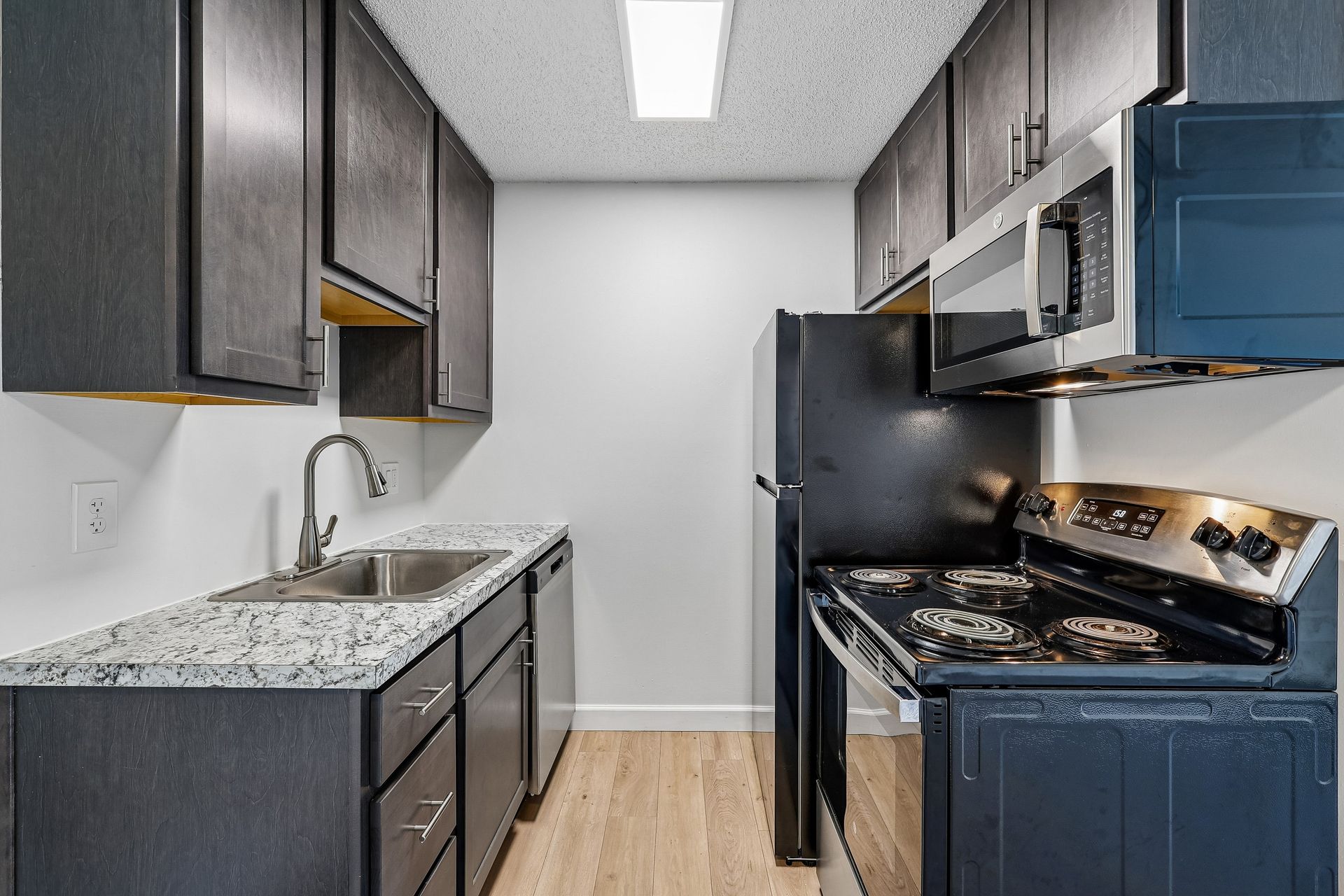 Tall Timber Apartments kitchen with espresso cabinets, gray countertops, stainless sink, and black stove and microwave.