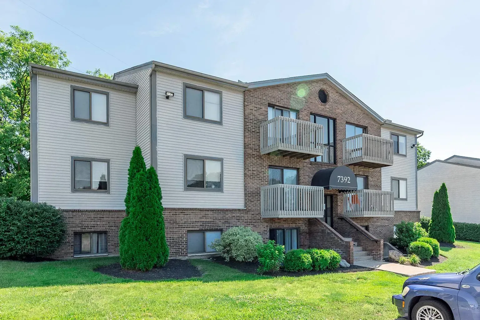 Tall Timber Apartments Exterior view of a two-story apartment building with brick facade, balconies, and a green lawn.