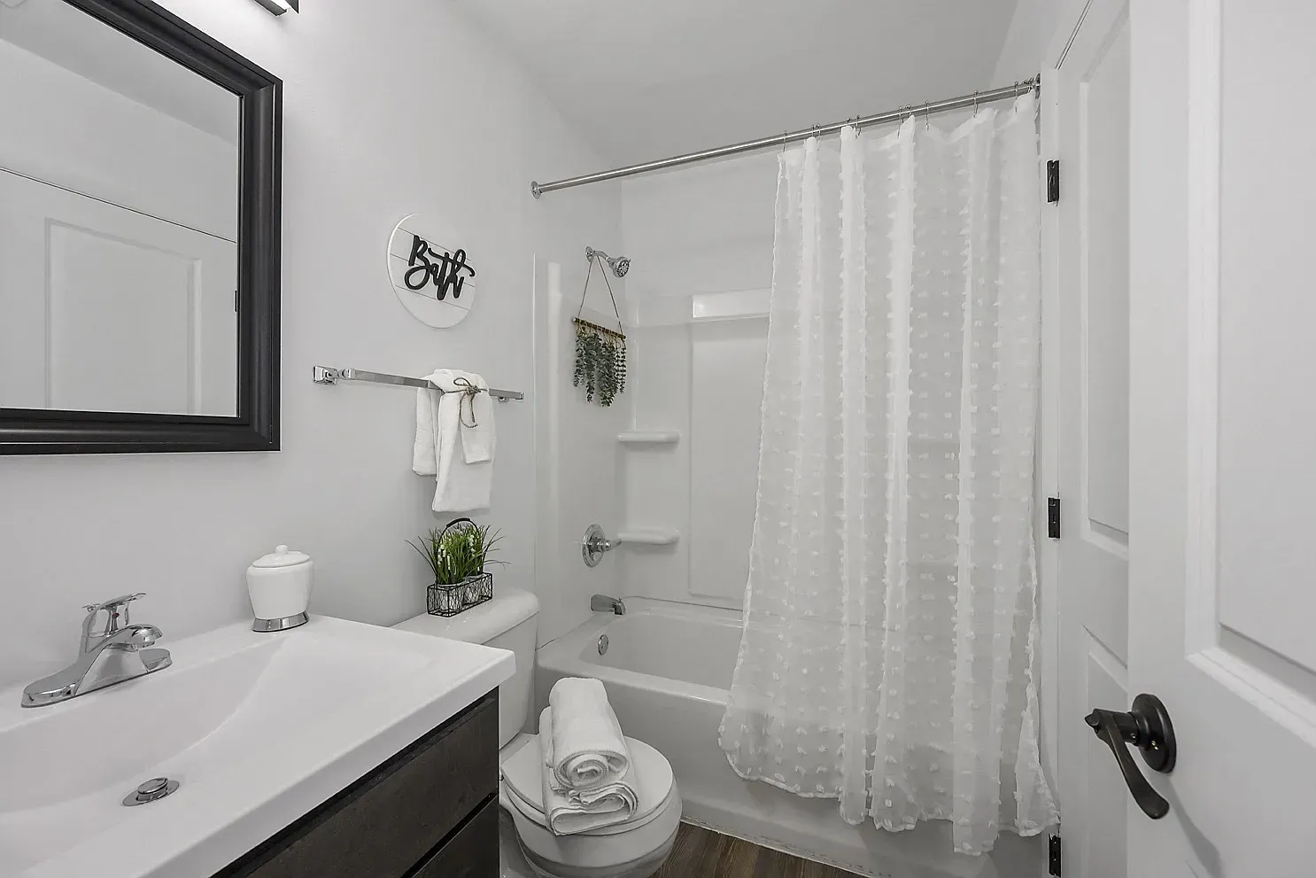 Tall Timber Apartments Bathroom with white sink, mirror, toilet, and tub with a white shower curtain.