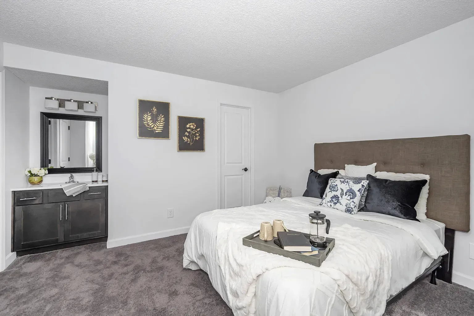 Tall Timber Apartments Bedroom with a large bed, upholstered headboard, and a vanity area with mirror.