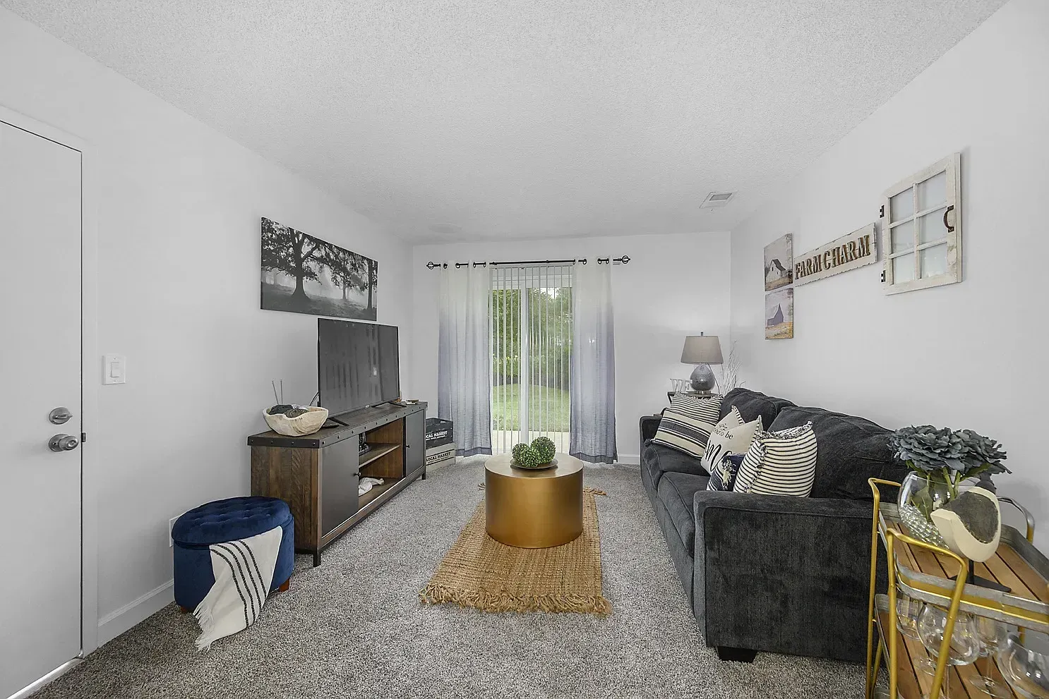 Tall Timber Apartments Living room in an apartment with a sofa, TV stand, circular coffee table, and sliding glass door.