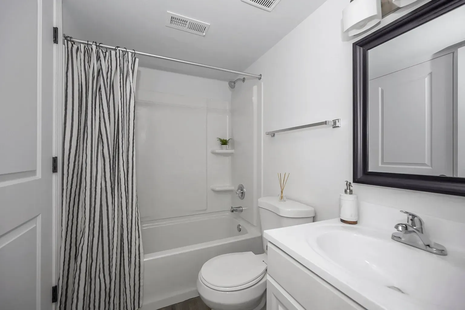 Tall Timber Apartments White apartment bathroom with a tub/shower, toilet, vanity, and mirror.