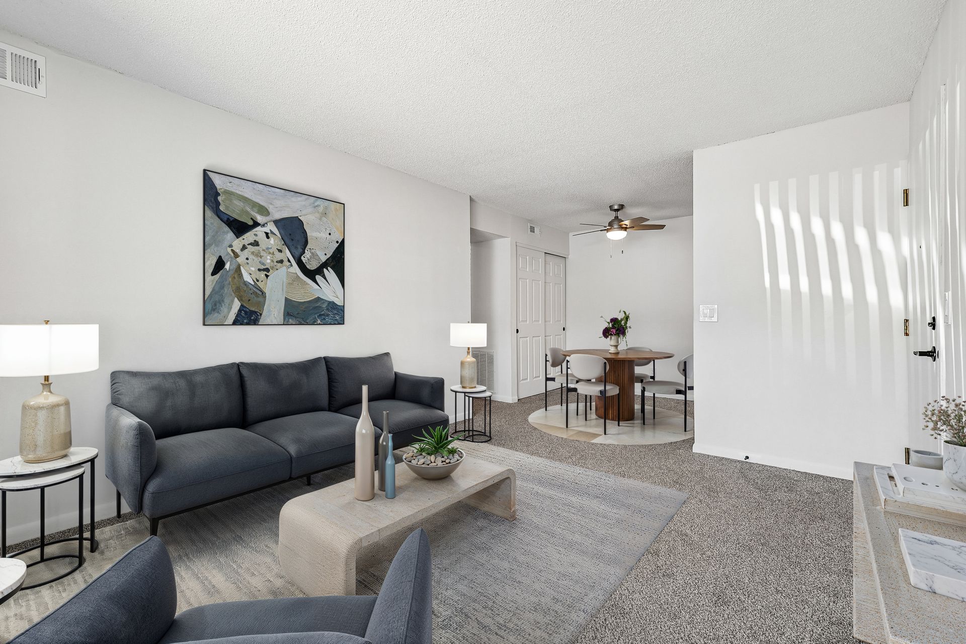 Tall Timber Apartments Bright living room with sofa, armchair, coffee table, wall art, and dining area beyond.