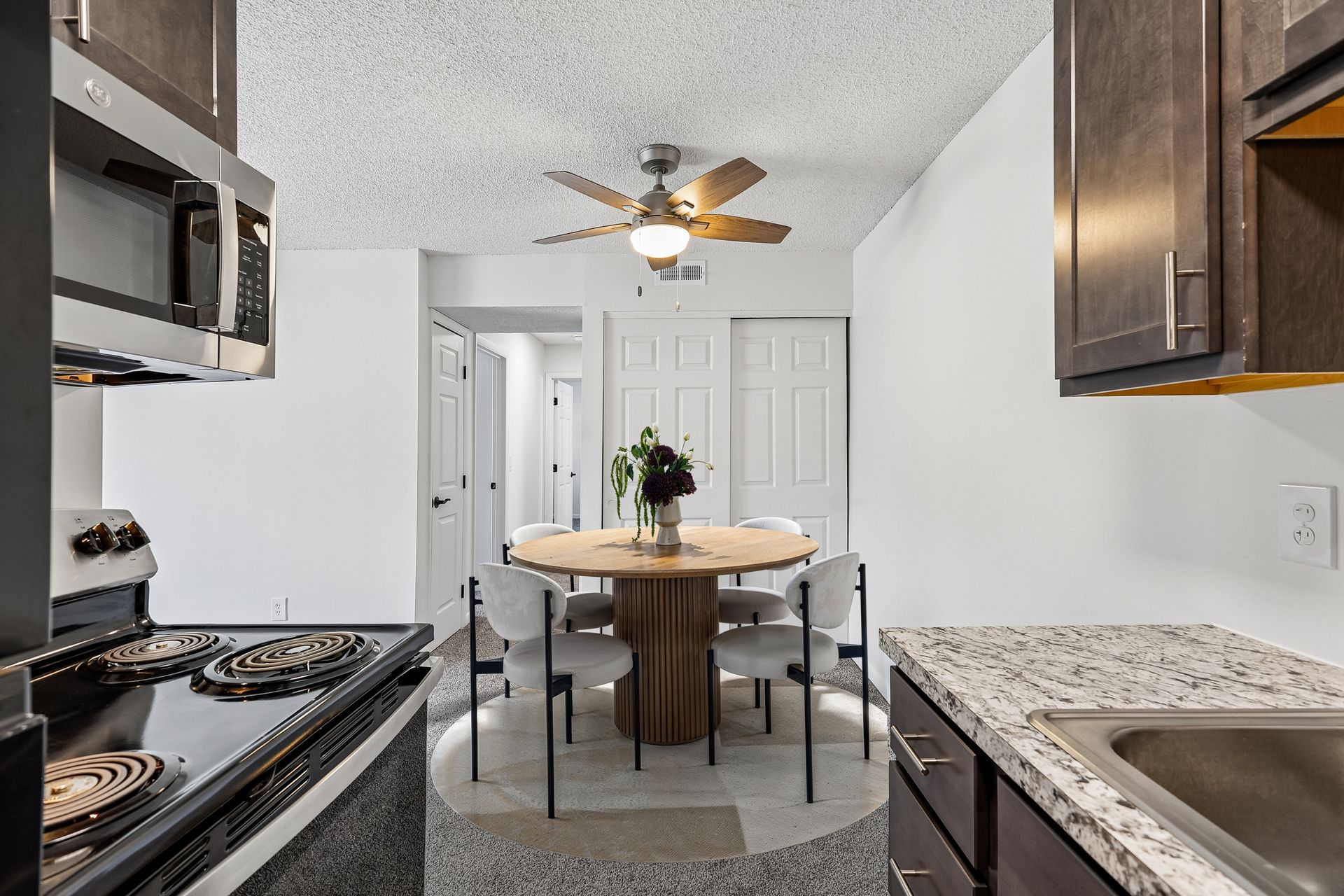 Tall Timber Apartments kitchen with white walls, dark cabinets, granite counters, and a round dining table by a ceiling fan.