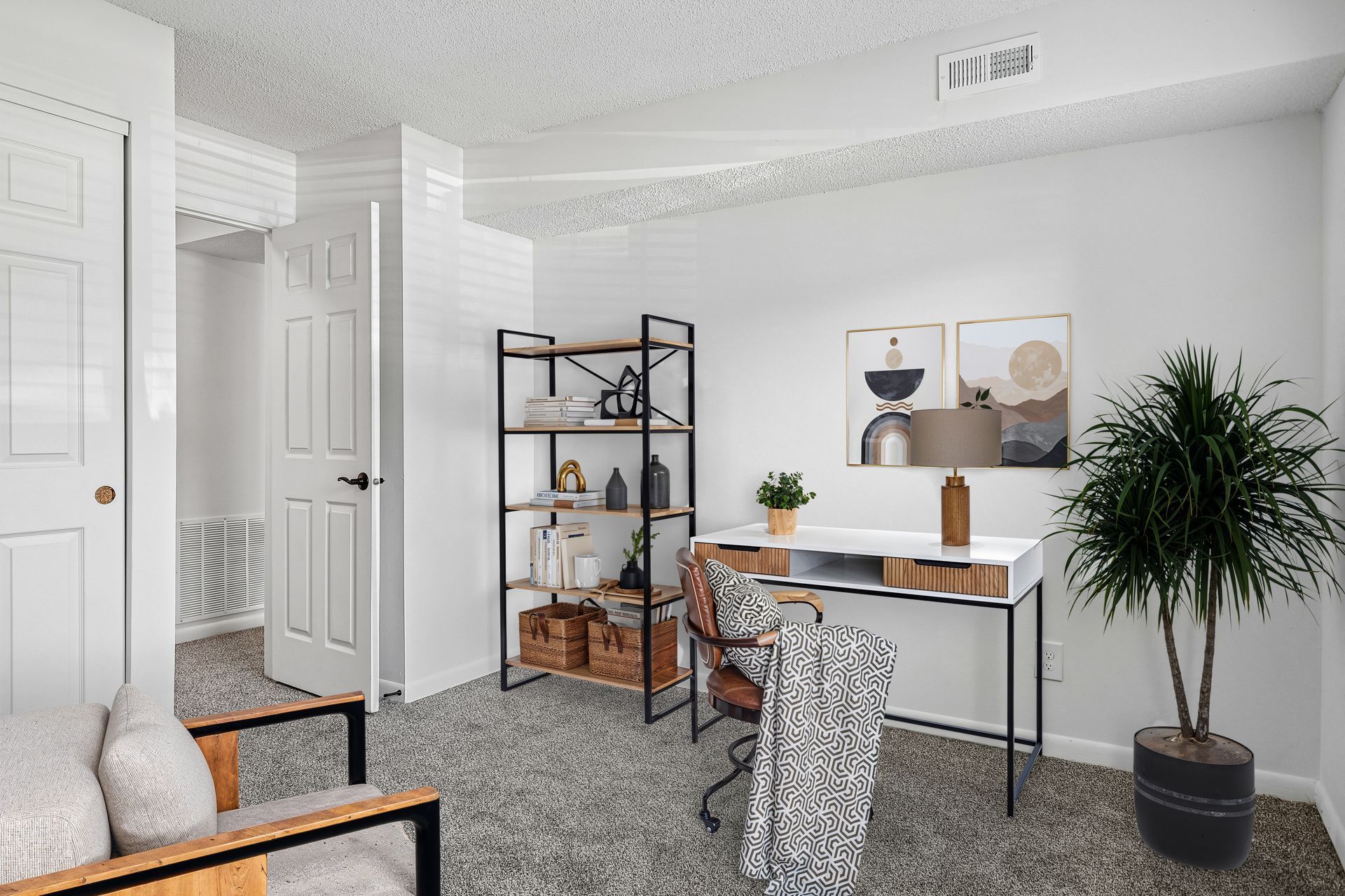 Tall Timber Apartments Bright home office with desk, shelving, chair, large plant, and abstract wall art on white walls