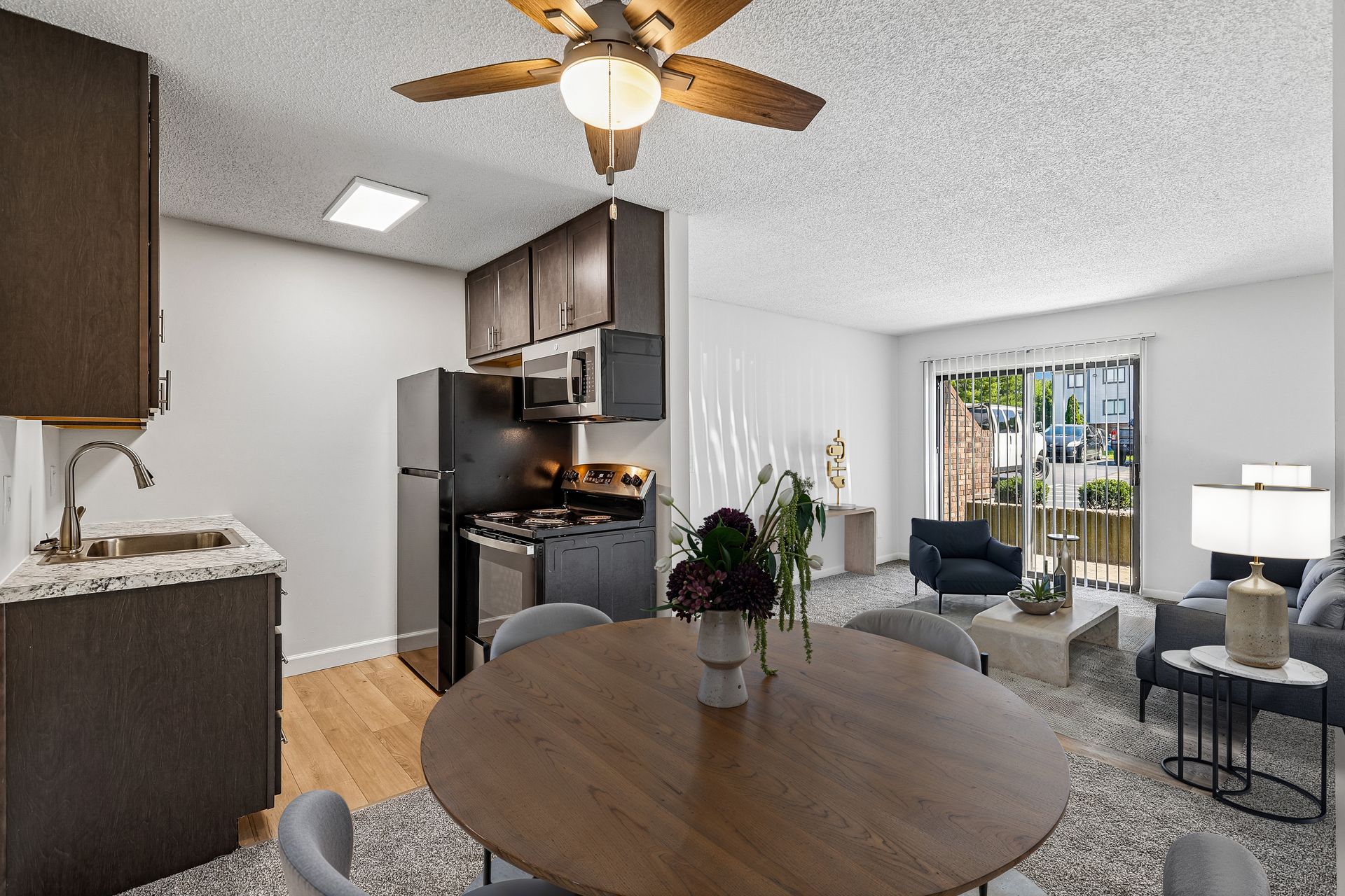 Tall Timber Apartments kitchen and living room with dark cabinets, round table, and sliding glass door.