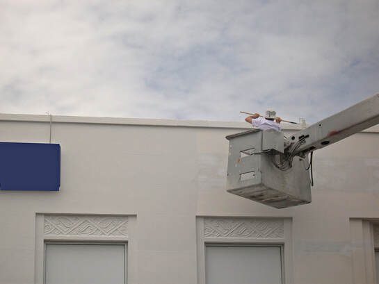 Utility bucket lift extended over a white building under a cloudy sky