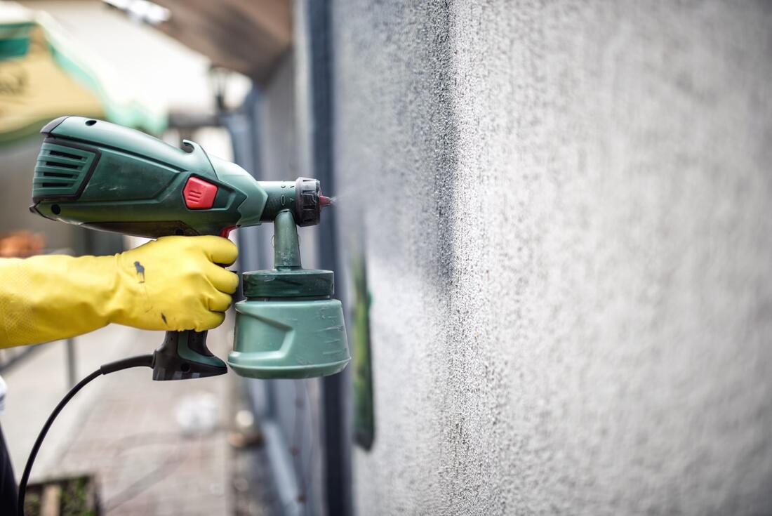 Handheld green spray gun painting a wall, with a gloved hand holding it close to the surface