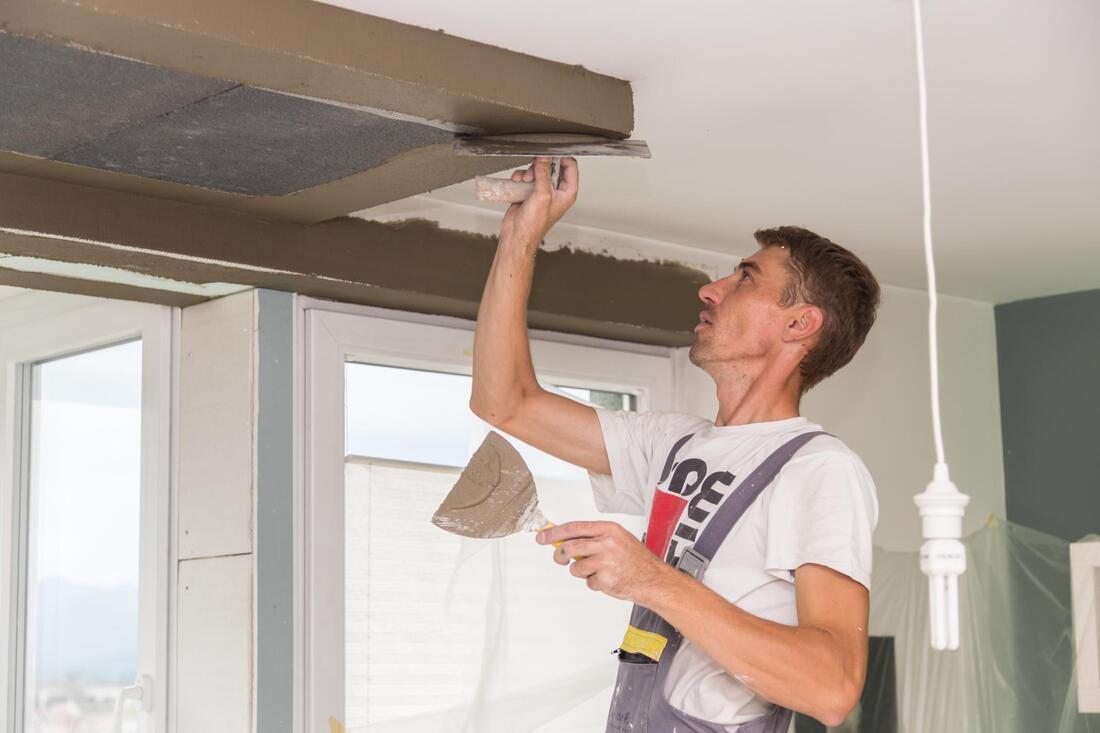Person painting or repairing a ceiling trim with a tool indoors near windows.