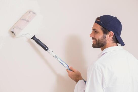 Man in a blue cap painting a white wall with a roller