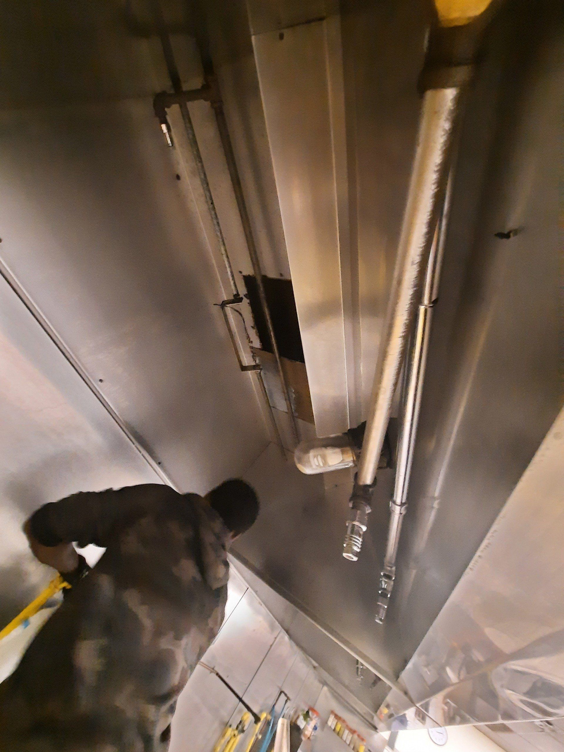 Une personne inspecte le système de ventilation métallique suspendu. À l'intérieur, on aperçoit les tuyaux et les conduits.
