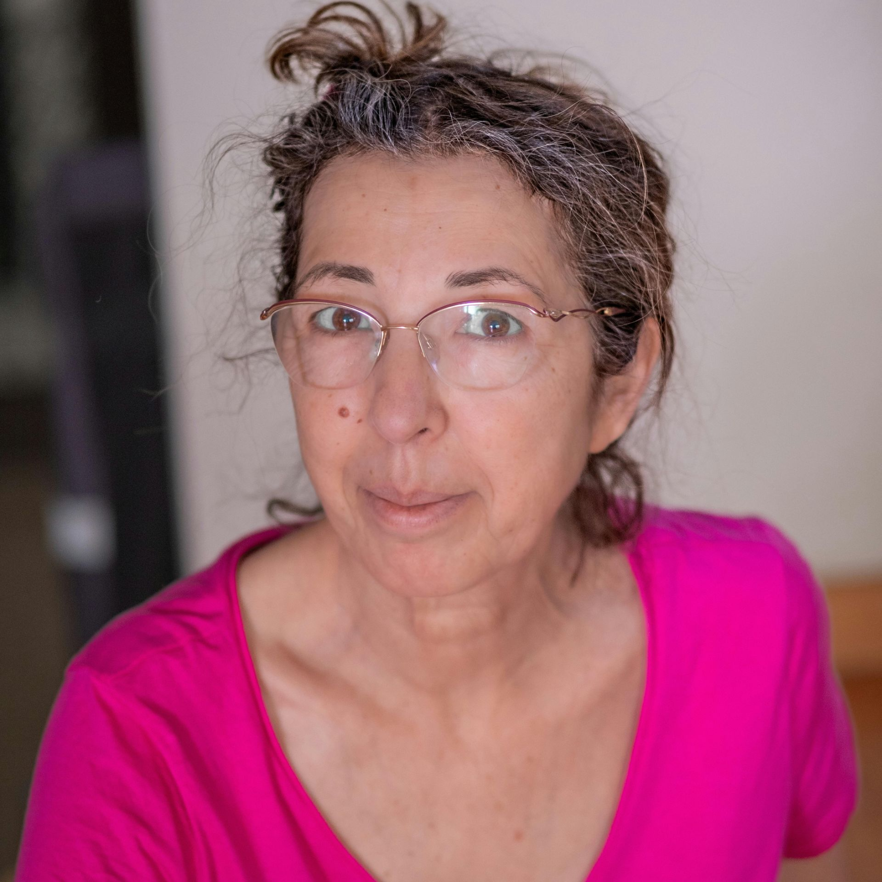 Woman with glasses and graying hair in a pink shirt, looking directly at the viewer.