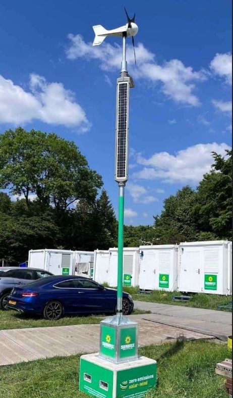Stazione meteorologica bianca con pannello solare e sensori su un palo metallico all'aperto, con montagne e cielo azzurro sullo sfondo.