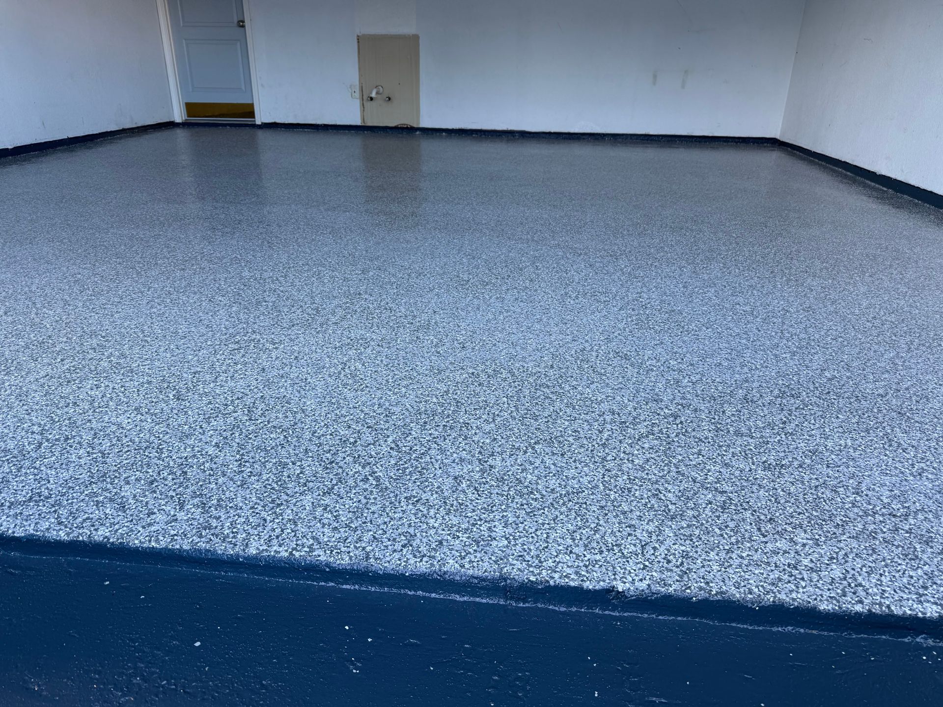 A garage with a shiny, speckled epoxy floor in shades of gray, white, and blue.