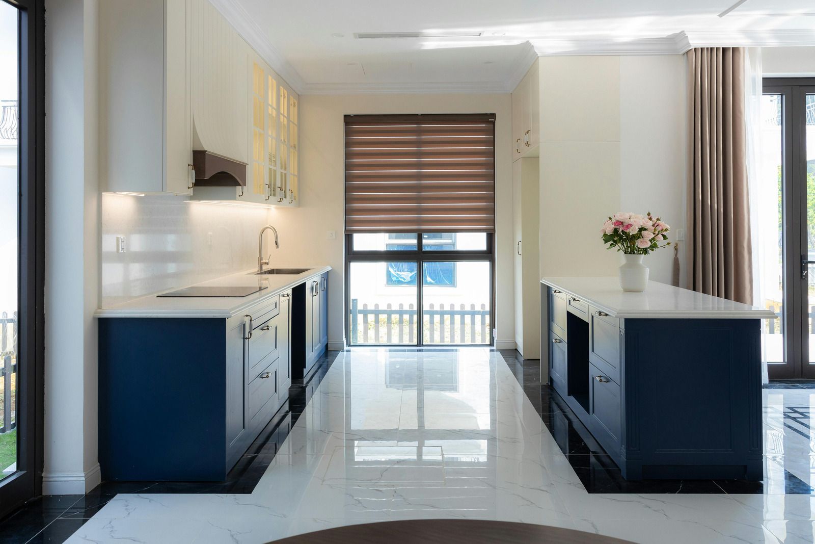 Modern kitchen with white and navy blue cabinets, marble countertops, and a central island.