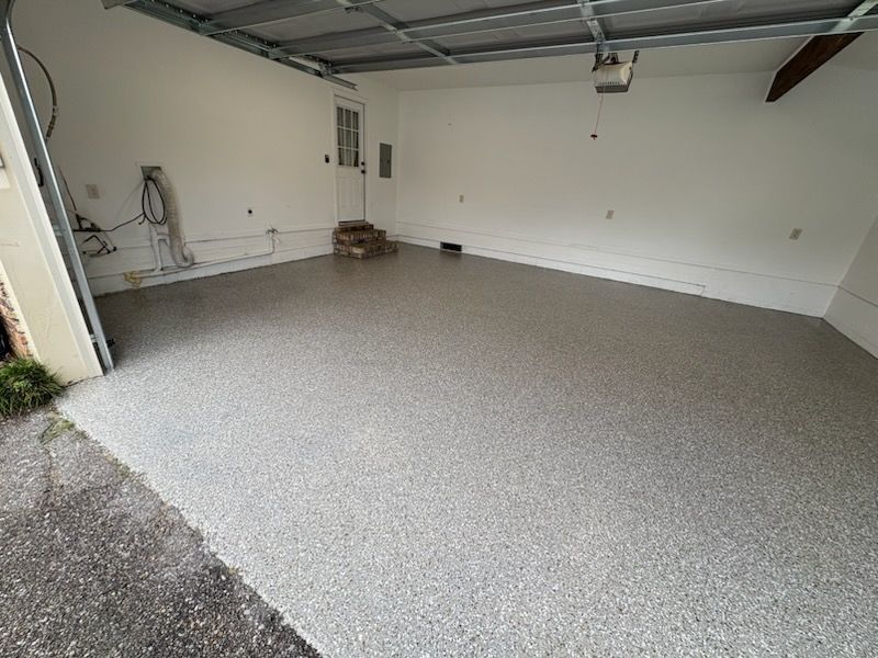 Empty garage with gray epoxy floor, white walls, and a small door at the back.